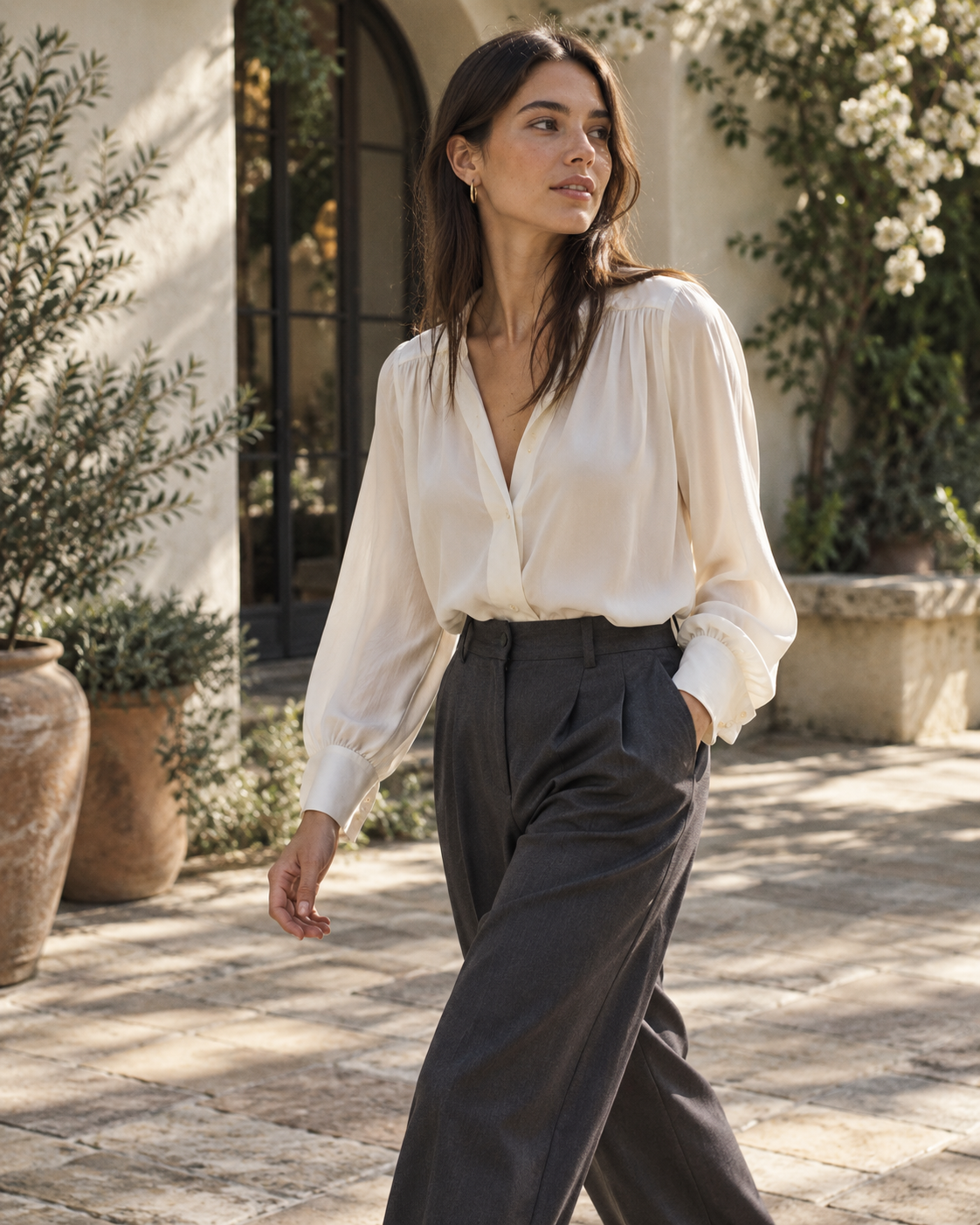Robin K editorial campaign: ivory blouse and charcoal trousers, candid side-glance in natural courtyard light.